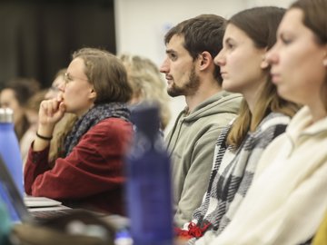 In einem Hörsaal sitzen Studierende in einer Reihe mit Laptops und Wasserflaschen auf den Tischen vor ihnen.