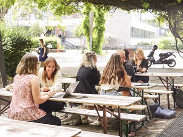 Eine Gruppe Studierender sitzt an Biertischen vor der caphete der Hochschule