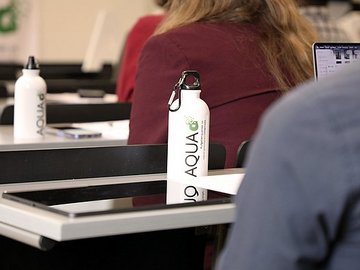 Impression der AQUA-d Konferenz - Flasche mit AQUA-d Logo auf einem Tisch im Hörsaal