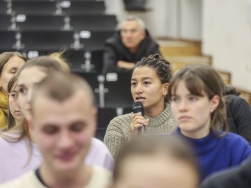 In einem Hörsaal spricht eine Studentin im Publikum in ein Mikrofon.