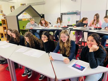 Schülerinnen sitzen im Lern-Lehr-Labor Mathematik an Tischen und betrachten Arbeitsblätter.