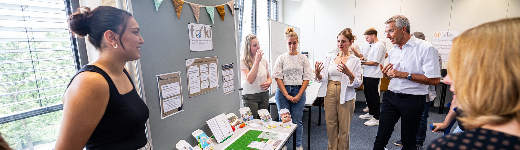 Studierendengruppen haben ihre Projekte aus dem Seminar Social Entrepreneurship in einem Seminarraum aufgebaut, die von den Jurymitgliedern begutachtet werden, u.a. vom damaligen Bürgermeister Martin Lenz.