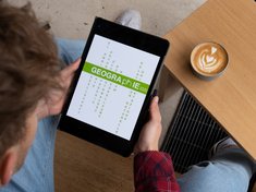 Es wird ein Tablet mit dem Logo des Faches gezeigt. Das Logo zeigt die Bedeutung von Geographie an der Pädagogischen Hochschule Karlsruhe, wie Raum mehrsprachig zwischen Gesellschaft und Umwelt verhandeln.