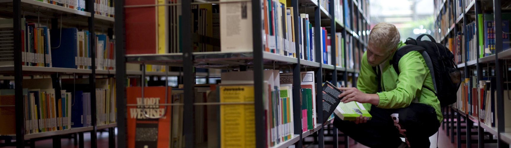 Ein Student sucht ein Buch in einem Bücherregal der Hochschulbibliothek
