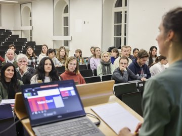 In einem Hörsaal hören Menschen einer Präsentation zu.