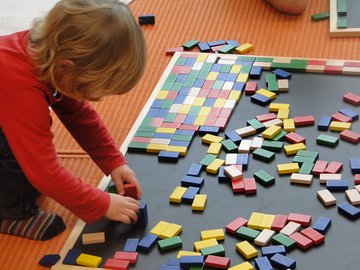 Ein Kind spielt auf dem Boden mit bunten Dominosteinen.