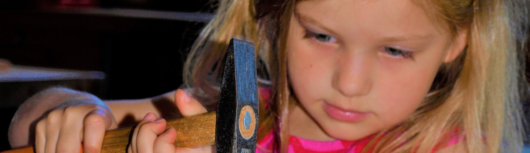 Ein Kindergartenkind schlägt mit einem Hammer einen Nagel ein