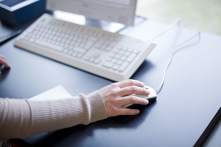 Ausschnitt eines Arms, dessen Hand auf einer Computermaus aufliegt. Davor ist eine Computertastatur der Bibliothek zu sehen. Die Bibliothek befindet sich im Gebäude 2 der PH Karlsruhe. 