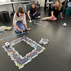 Drei Studentinnen sitzen im Z-LAB auf dem Boden und testen MINT-Materialien. Es sit eine Spielstraße aus mehreren Elementen auf den Boden gelegt