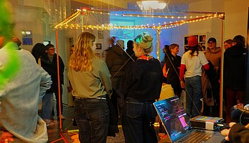 2026_02_11_Kunst im Jubez Situation auf der Kunstausstellung mit ein paar Personen, die eine Installation bettrachten, und weiteren im Hintergrund.