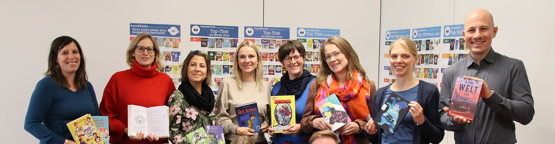 Eine Gruppe Menschen mit Büchern in den Armen und Bücherplakaten im Hintergrund.