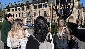 2025_Gruppe_Studiernde_vor_Gebäude_3 Drei Studentinnen und ein Student von hinten vor dem Gebäude 3 im Herbst