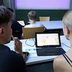 Zwei Schüler:innen sitzen an einem Laptop und konstruieren eine Blume